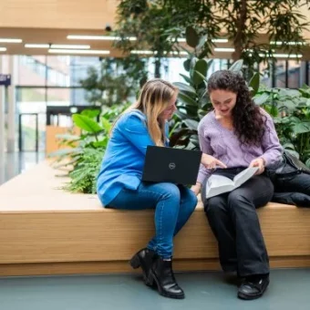 Campusfoto van Hogeschool Leiden met twee studenten die samen naar een laptopscherm kijken.